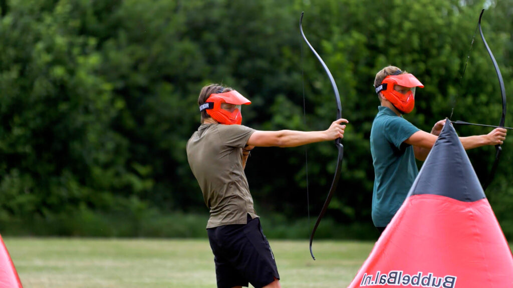 Twee spelers richten met pijl en boog tijdens een outdoor Archery Attack spel met beschermmaskers